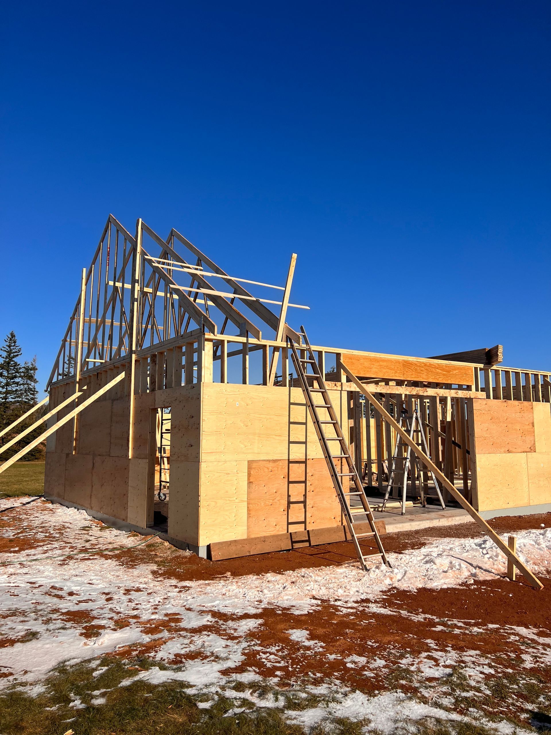 A house is being built in a snowy field with a blue sky in the background.