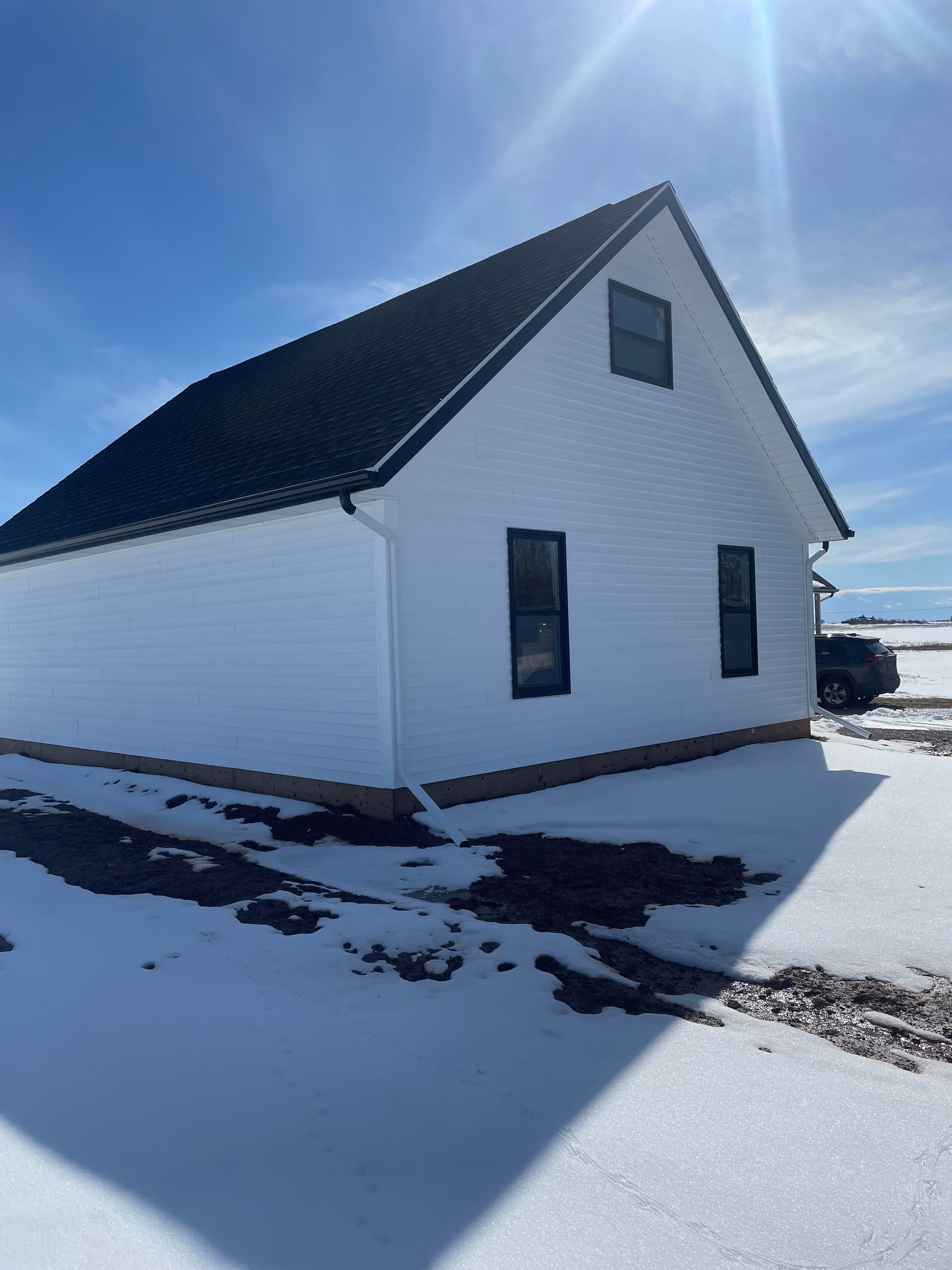 A white house with a black roof is surrounded by snow