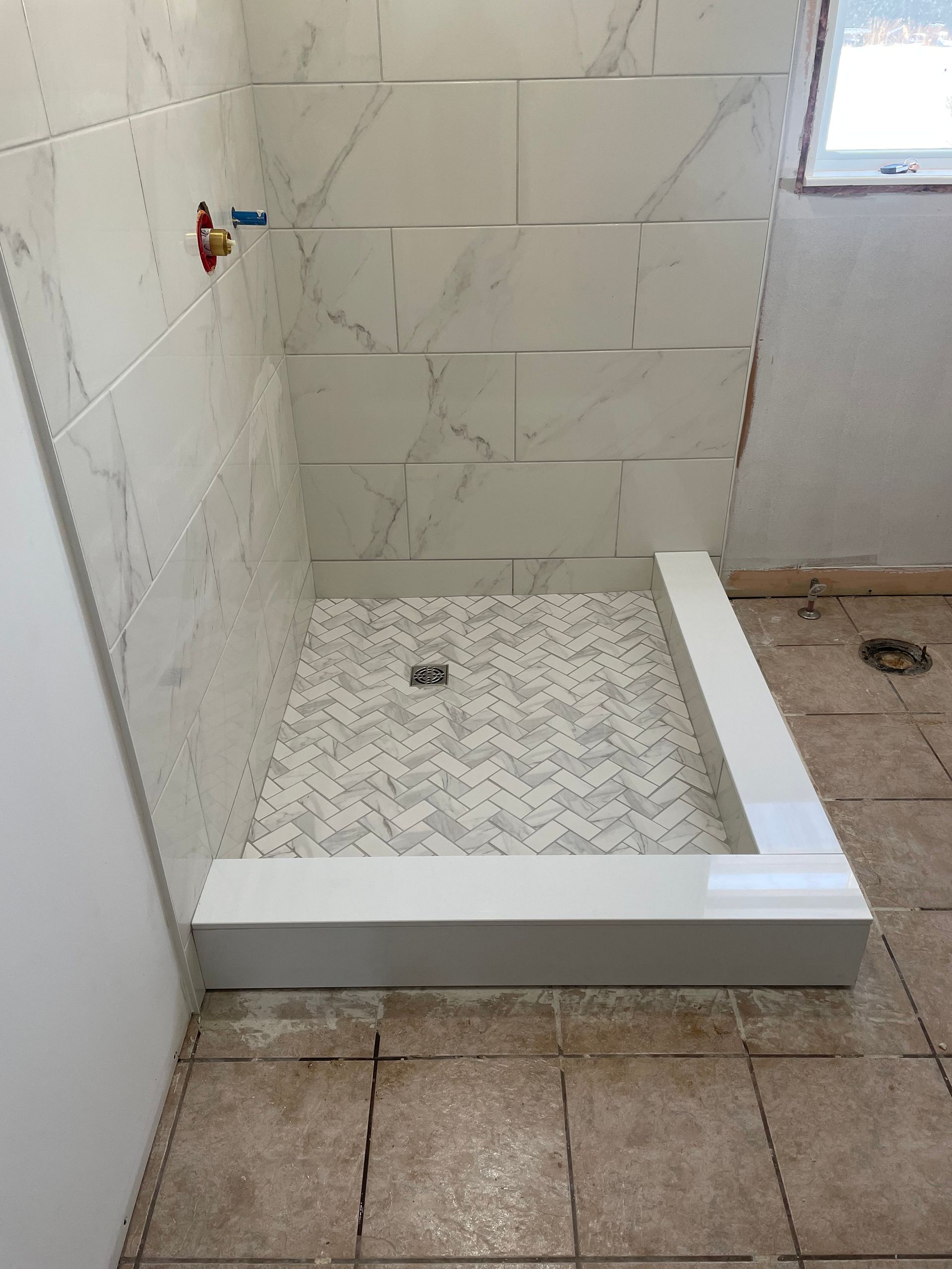 A bathroom with a tiled shower stall and a window.