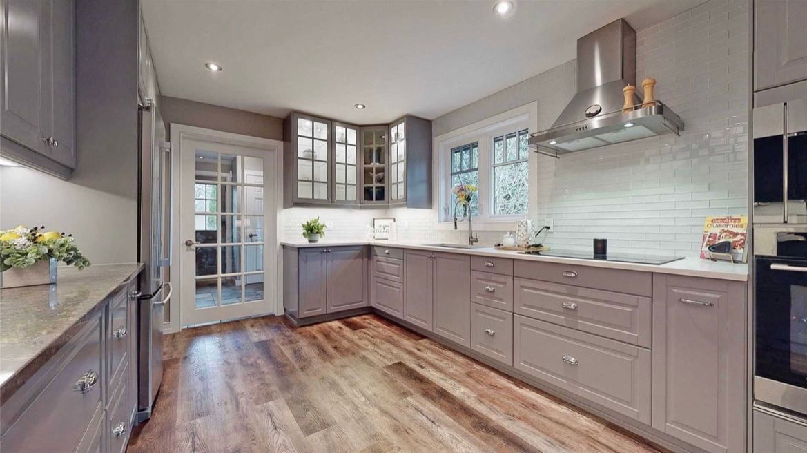 A kitchen with gray cabinets , stainless steel appliances , and hardwood floors.