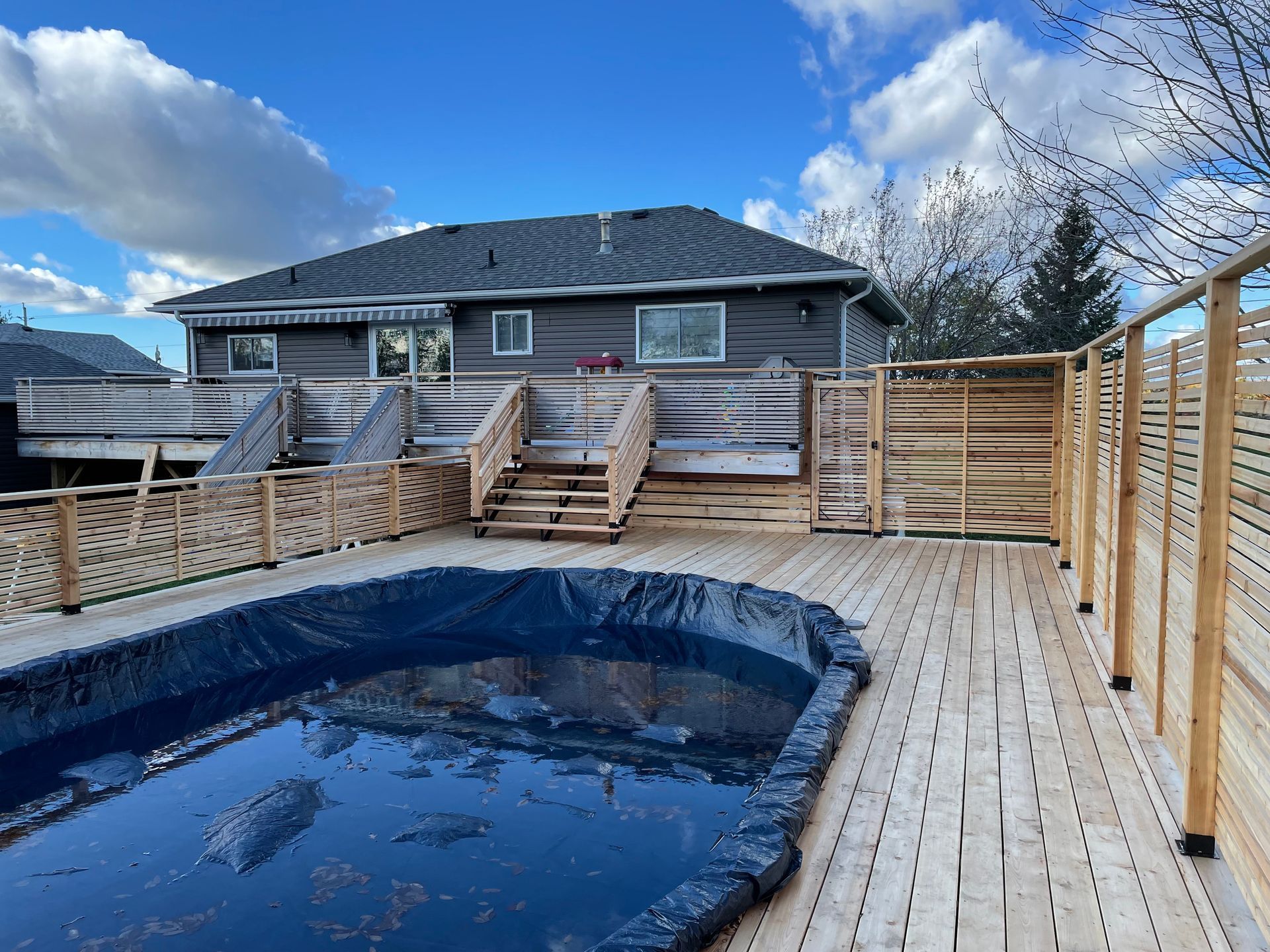 A wooden deck with a swimming pool and a house in the background.