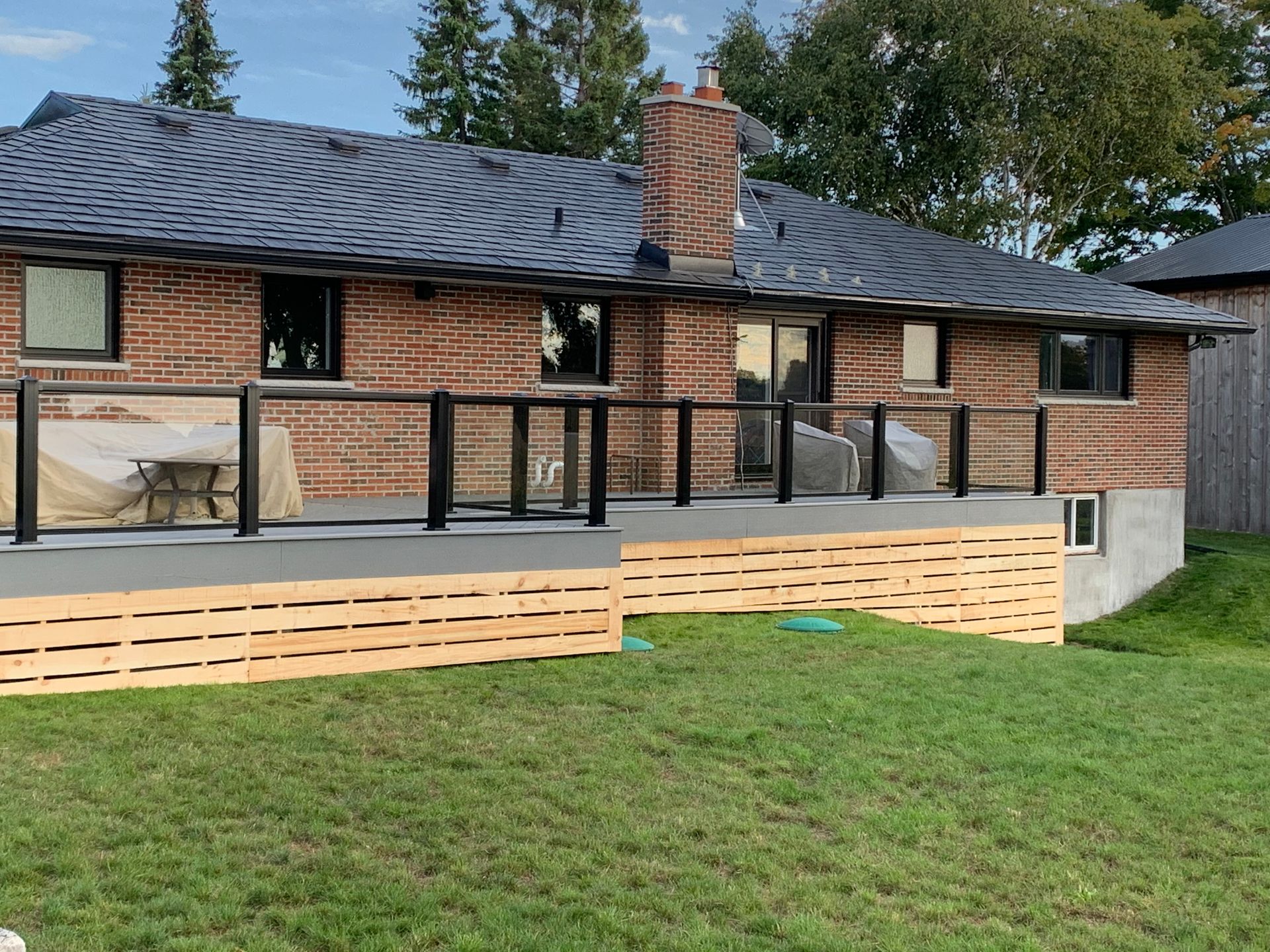 A brick house with a deck and a glass railing in the backyard.