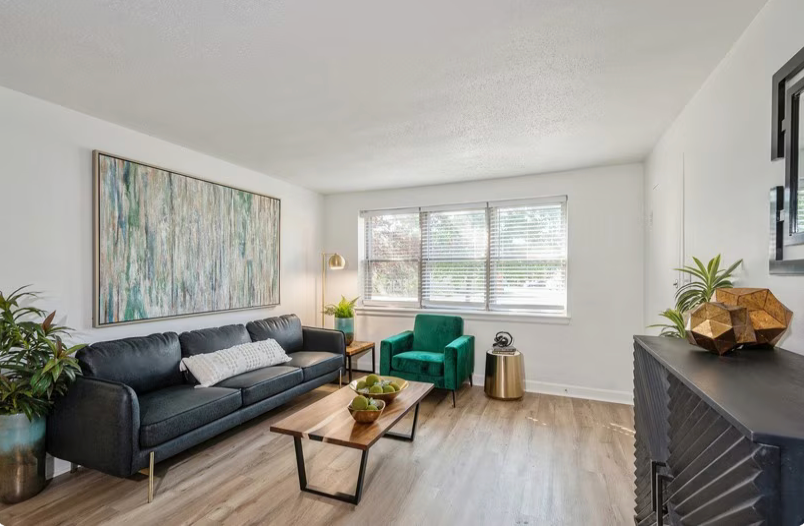 Living room with black sofa, green armchair, art, wood floor, and plants.