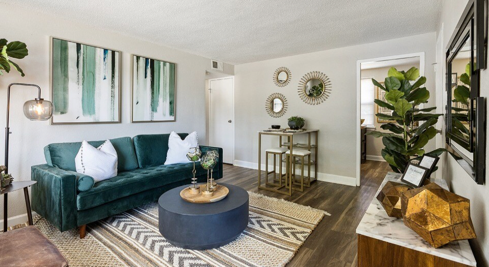 Living room with teal sofa, abstract art, gold accents, and hardwood floors.