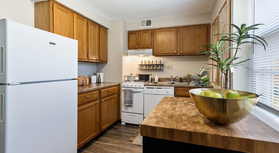 Kitchen with white appliances, wood cabinets, butcher block counter, and bowl of fruit.