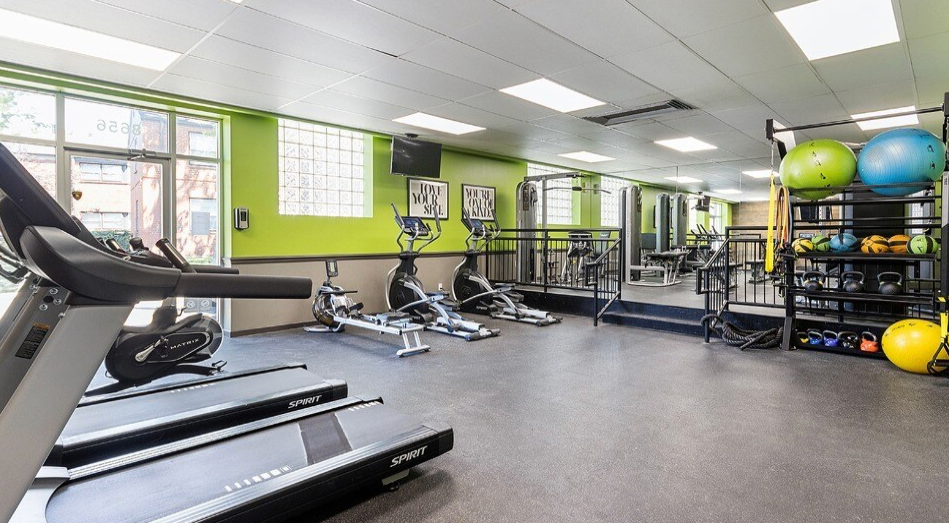 Gym interior with treadmills, rowing machines, weights, exercise balls, and a mirror.