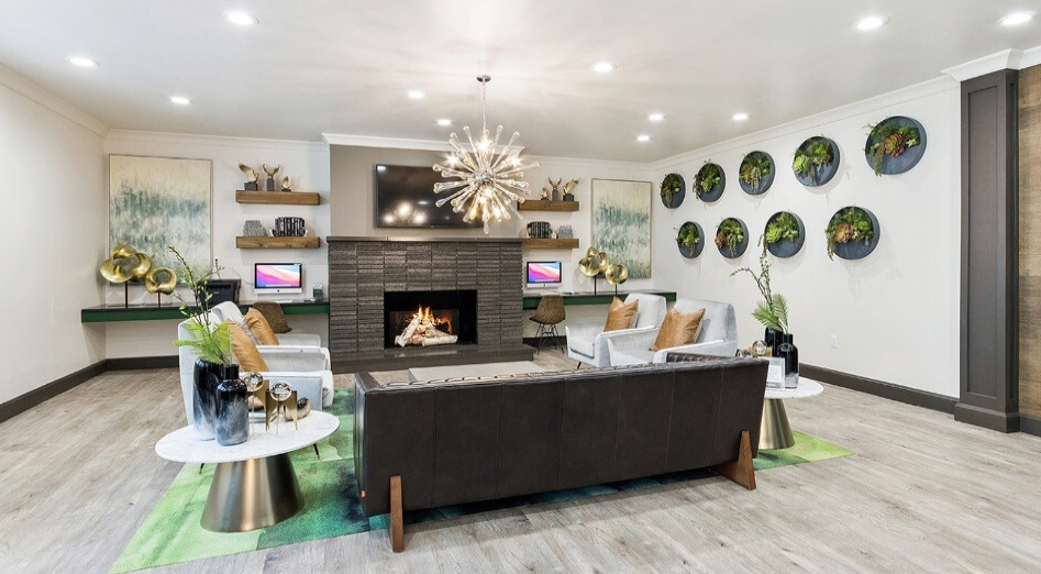 Cozy lounge with fireplace, sofas, green rug, and round tables. Living green wall and a chandelier.