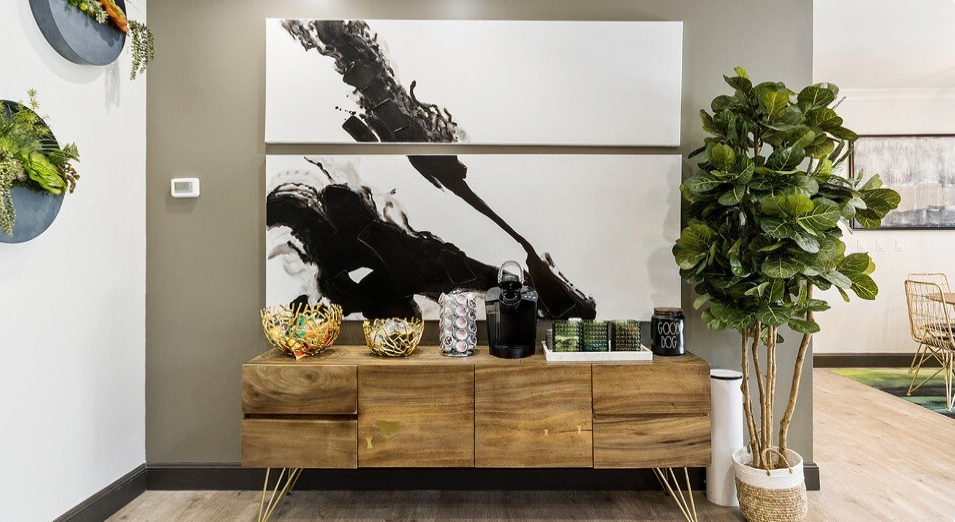Wooden console table with decor, large black and white abstract art, and a potted tree.