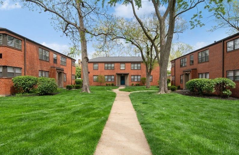 Red brick apartment buildings with green lawn and a pathway.