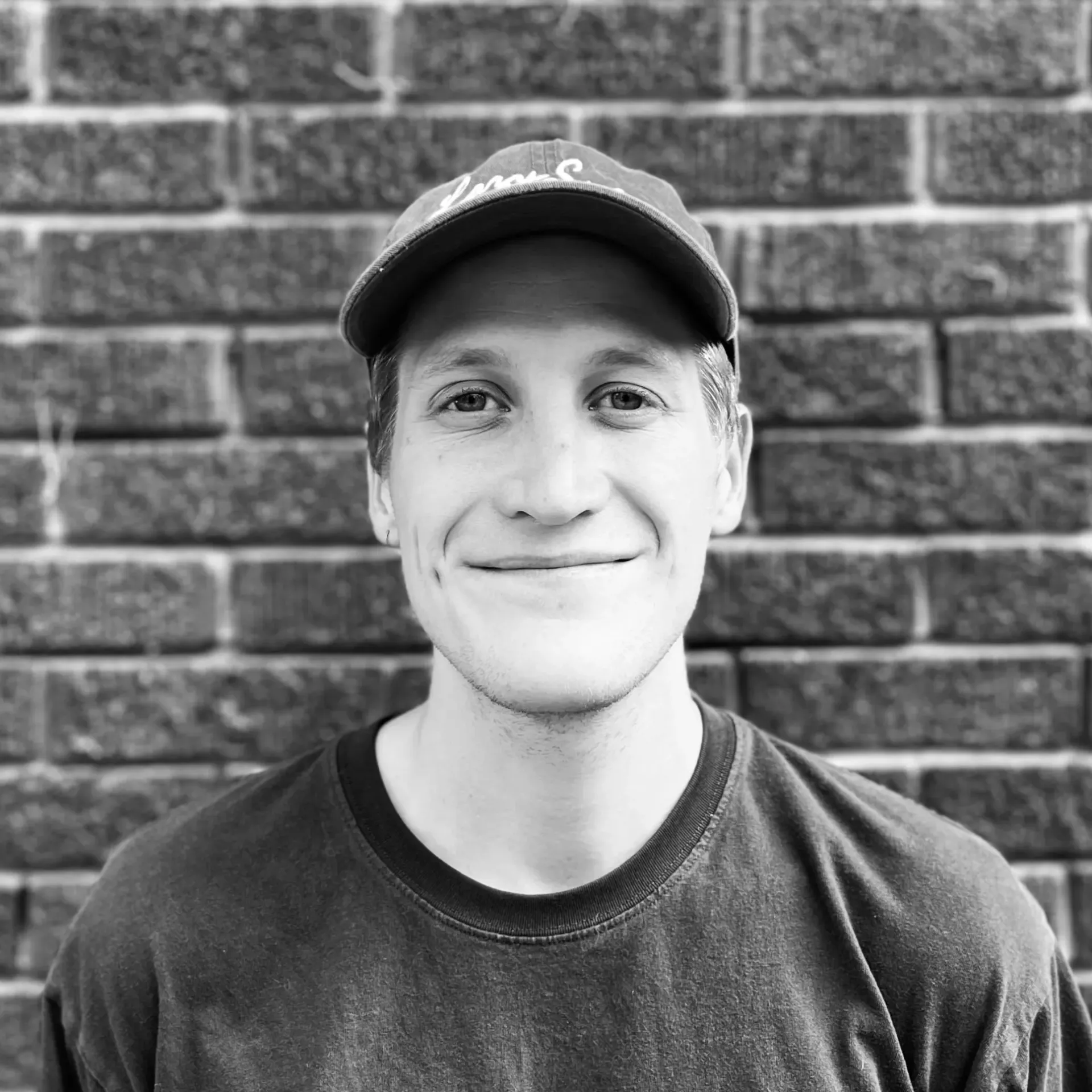 Man wearing a baseball cap and polo shirt, smiling at the camera in a studio.