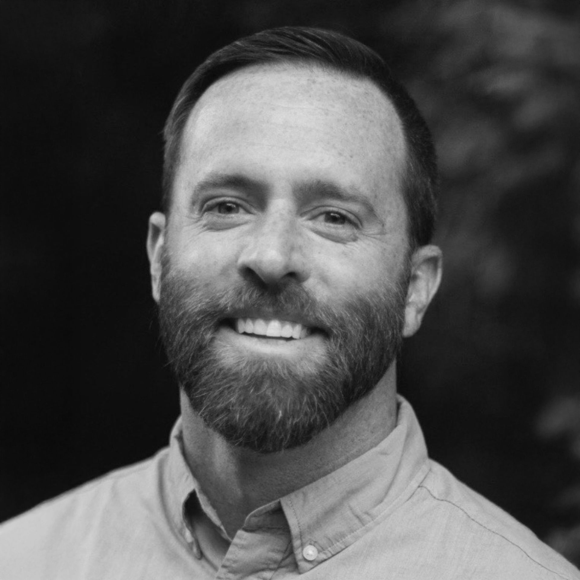Man wearing a baseball cap and polo shirt, smiling at the camera in a studio.