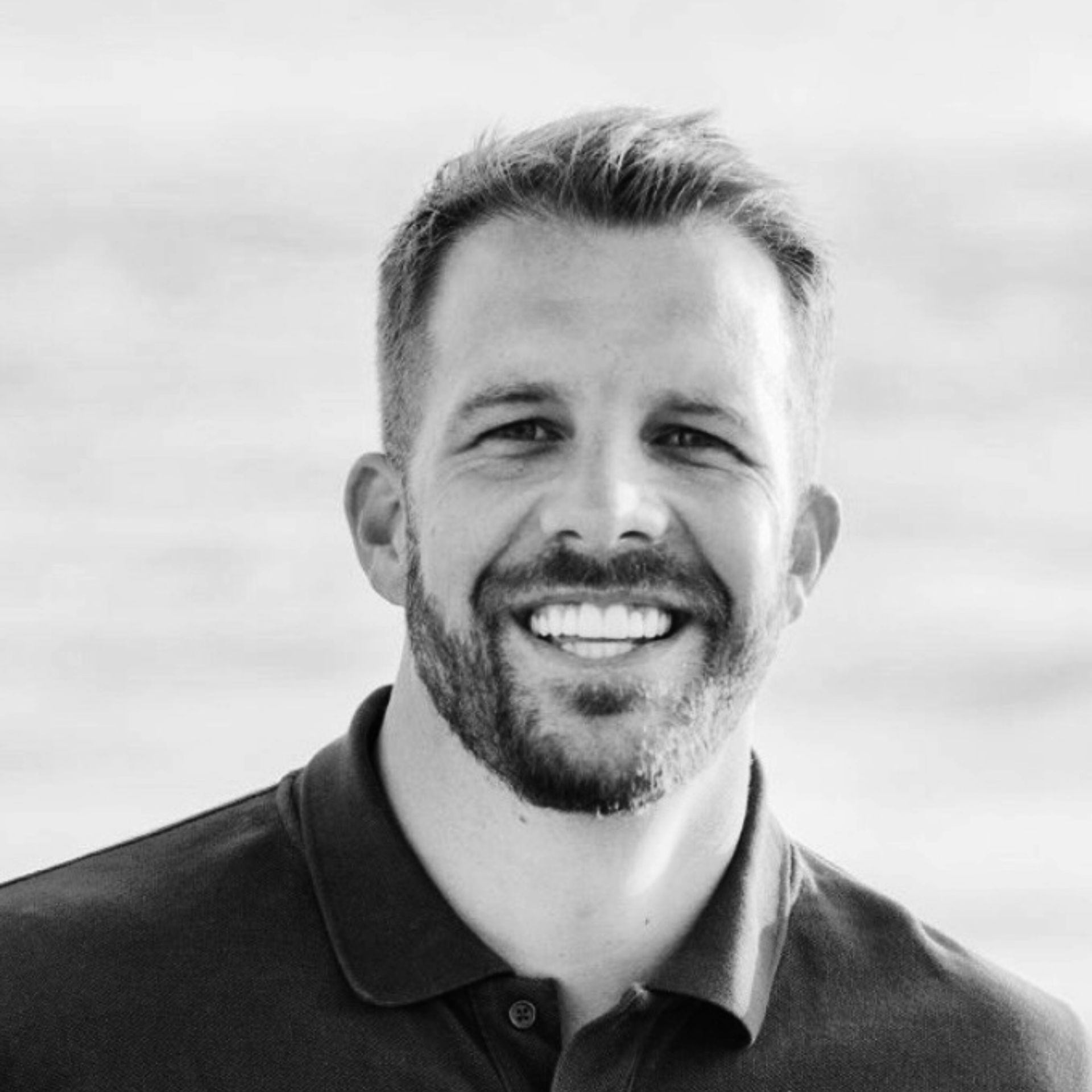 Man with beard smiling, wearing a dark polo shirt with a logo.