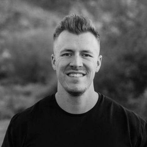 Man with short, styled hair, mustache, and goatee smiling in a black and white photo. Wearing a polo shirt.