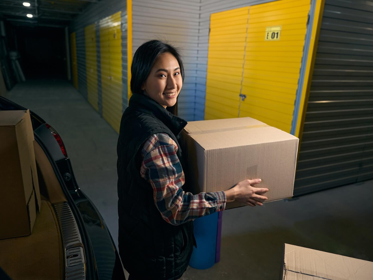 Woman carrying a cardboard box in a storage hallway with yellow unit doors