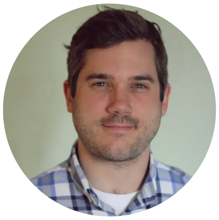 Man in blue plaid shirt smiles at the camera, light green background.