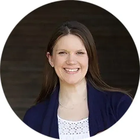 Woman smiling, wearing a navy cardigan over a white top. Brown hair. Dark background.