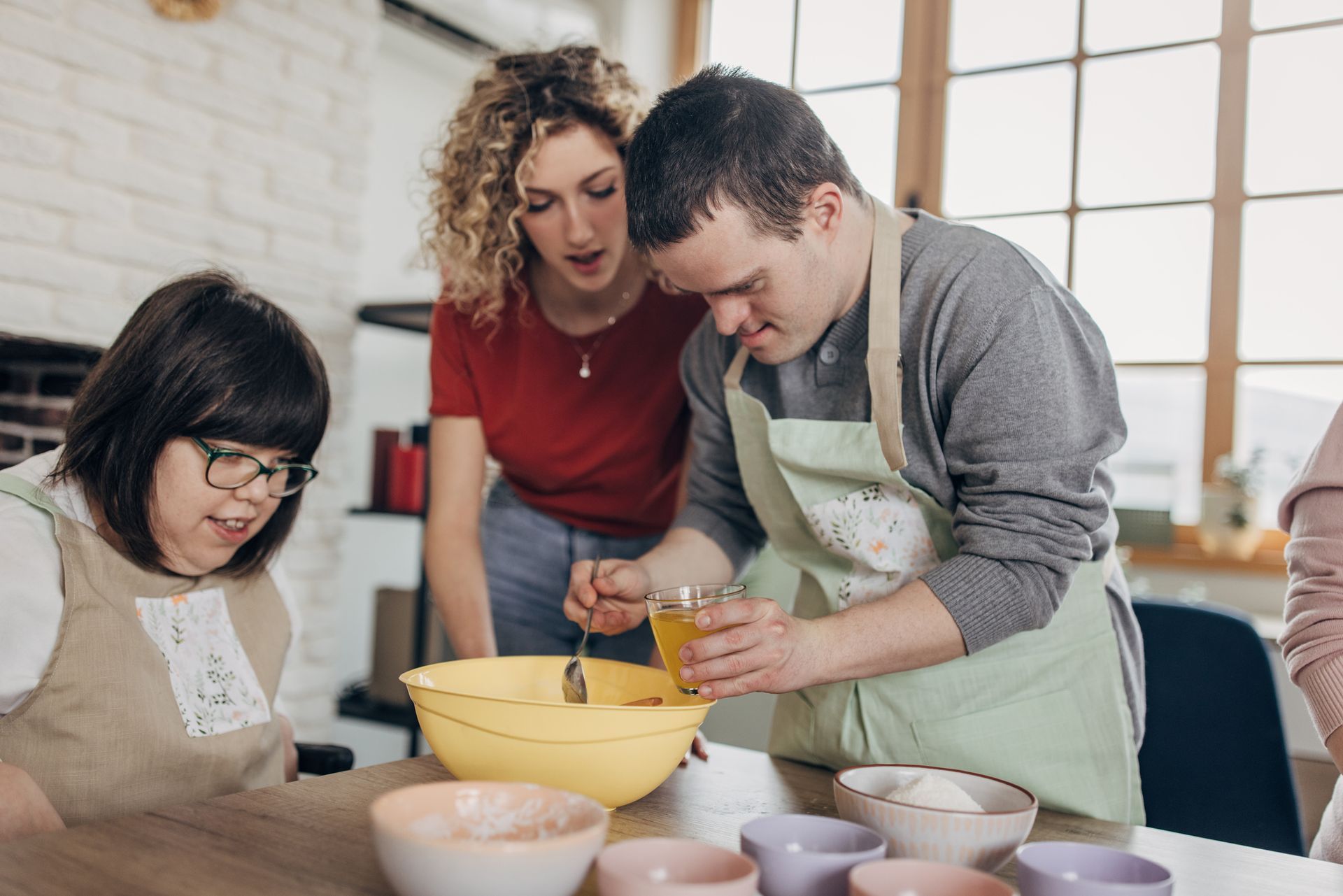 Three people cook in a kitchen: one stirs a bowl, two look on.