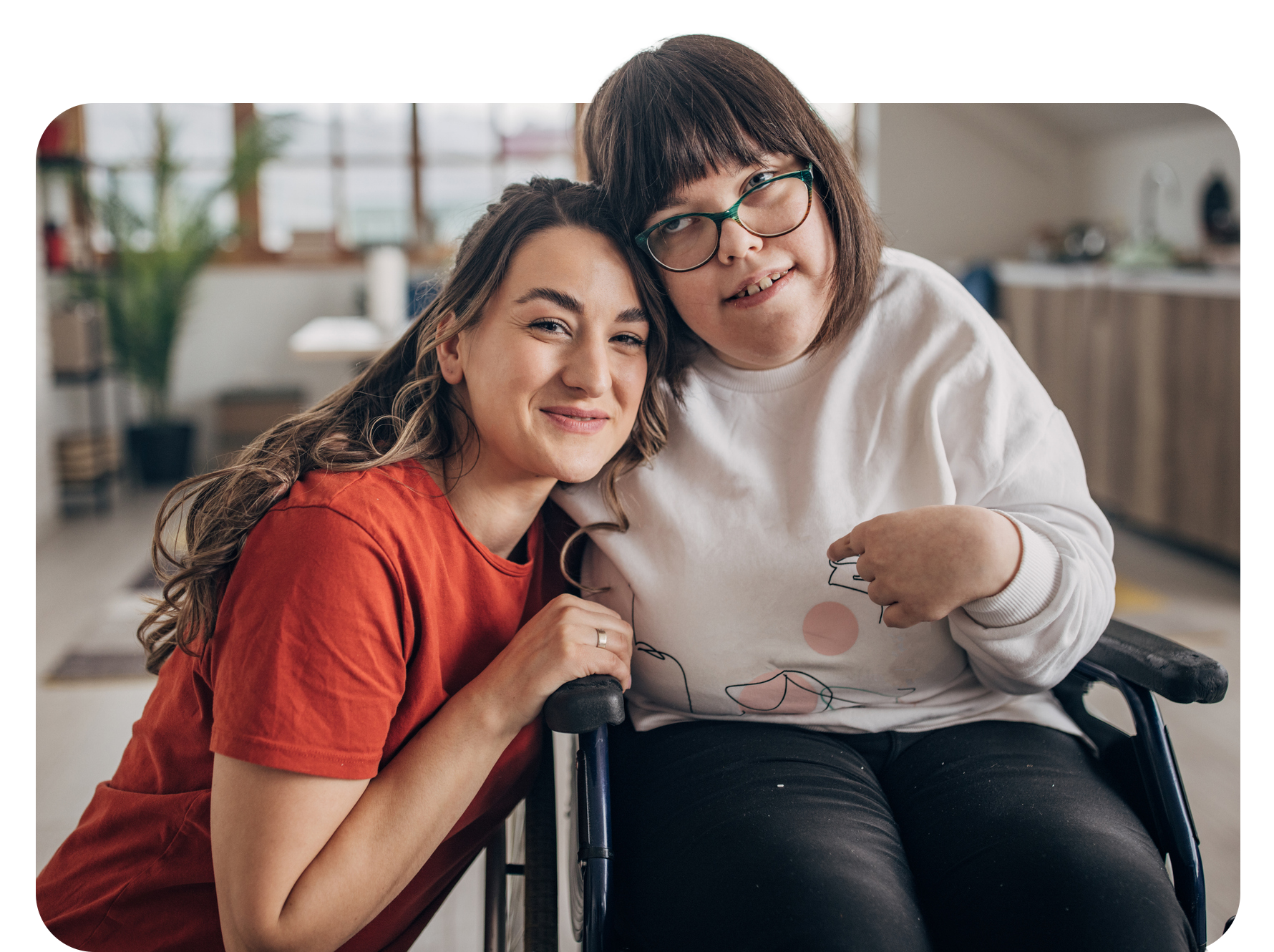 Woman in wheelchair smiles with another woman who has her arm around her.