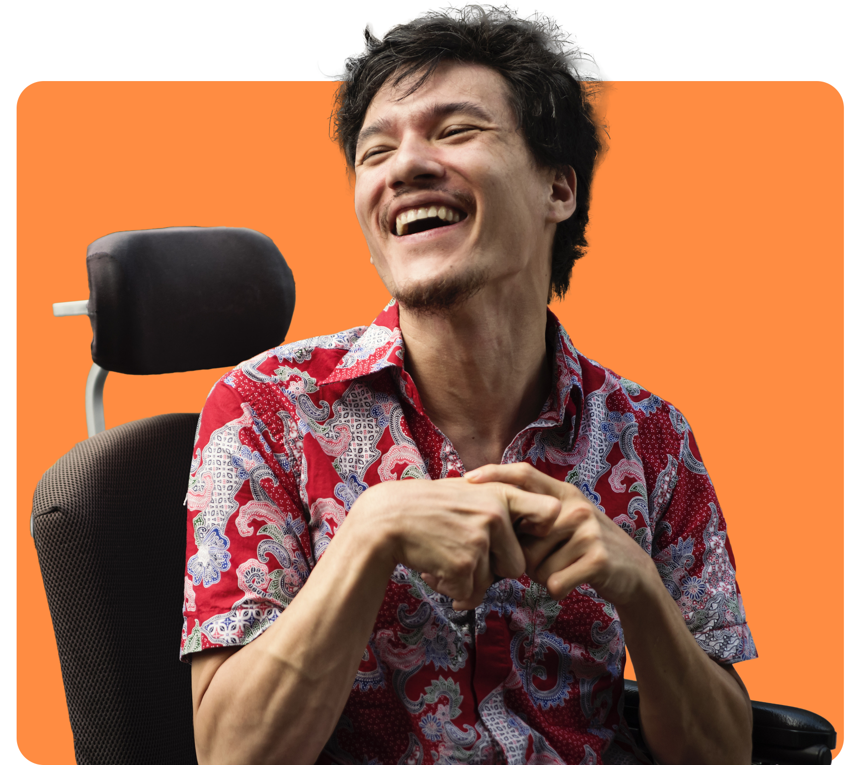 Man in wheelchair, smiling broadly, wearing red patterned shirt, orange background.