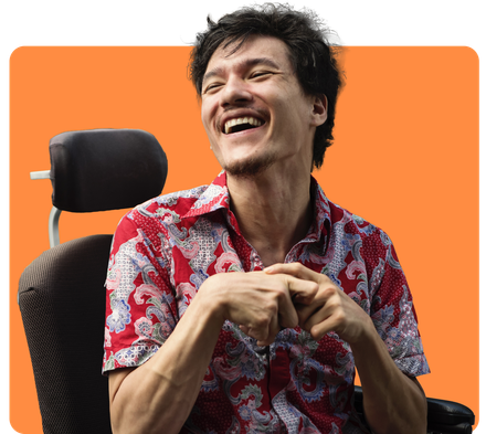 Man in wheelchair, smiling broadly, wearing red patterned shirt, orange background.