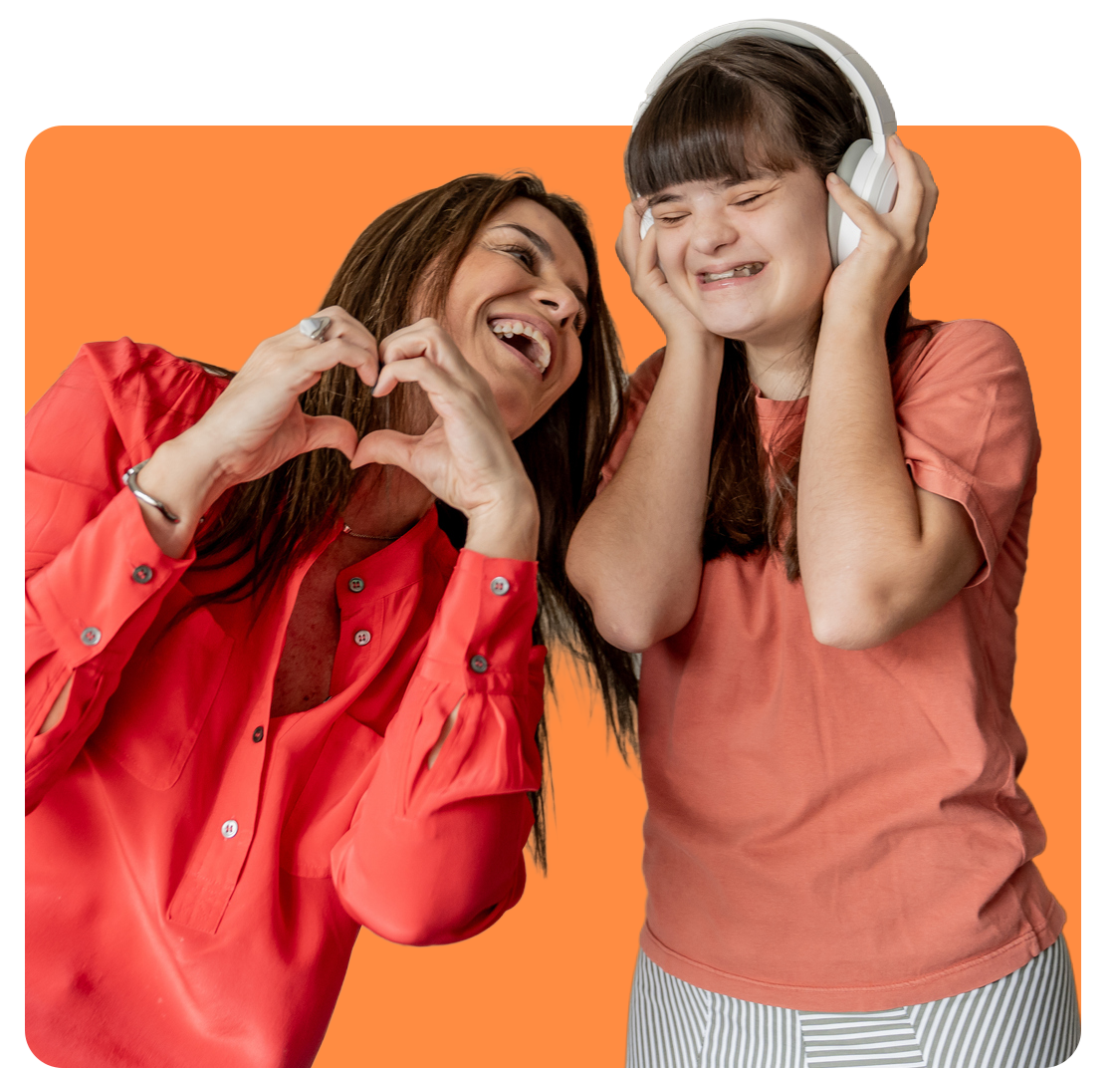 Woman forming a heart with hands, smiling at a person with Down syndrome wearing headphones and smiling.