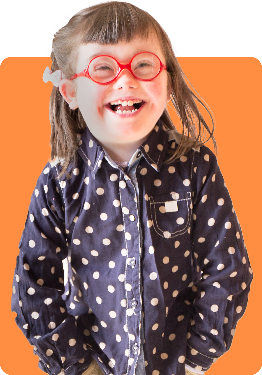 Girl with pigtails wearing glasses, a polka dot shirt, and khaki pants smiles with hands in pockets.