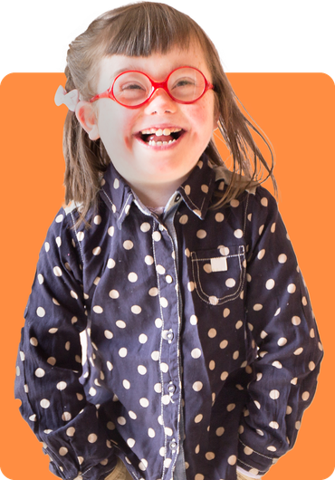 Girl with pigtails wearing glasses, a polka dot shirt, and khaki pants smiles with hands in pockets.