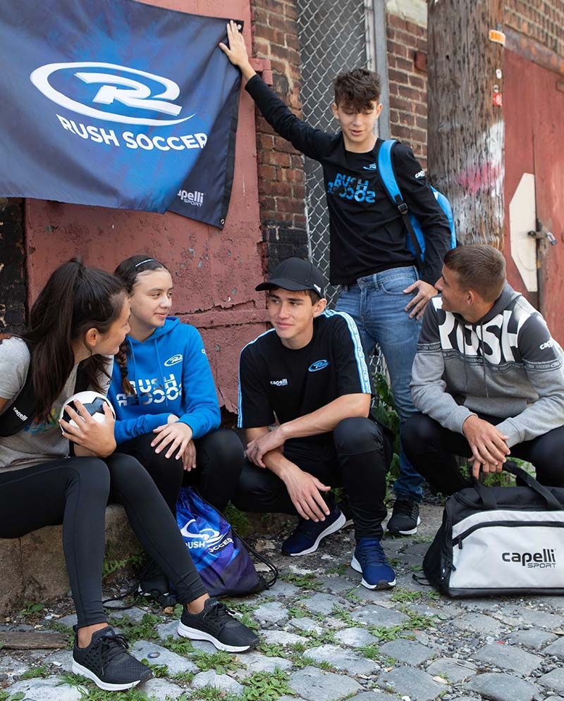 A group of young people are sitting on the sidewalk in front of a brick building.