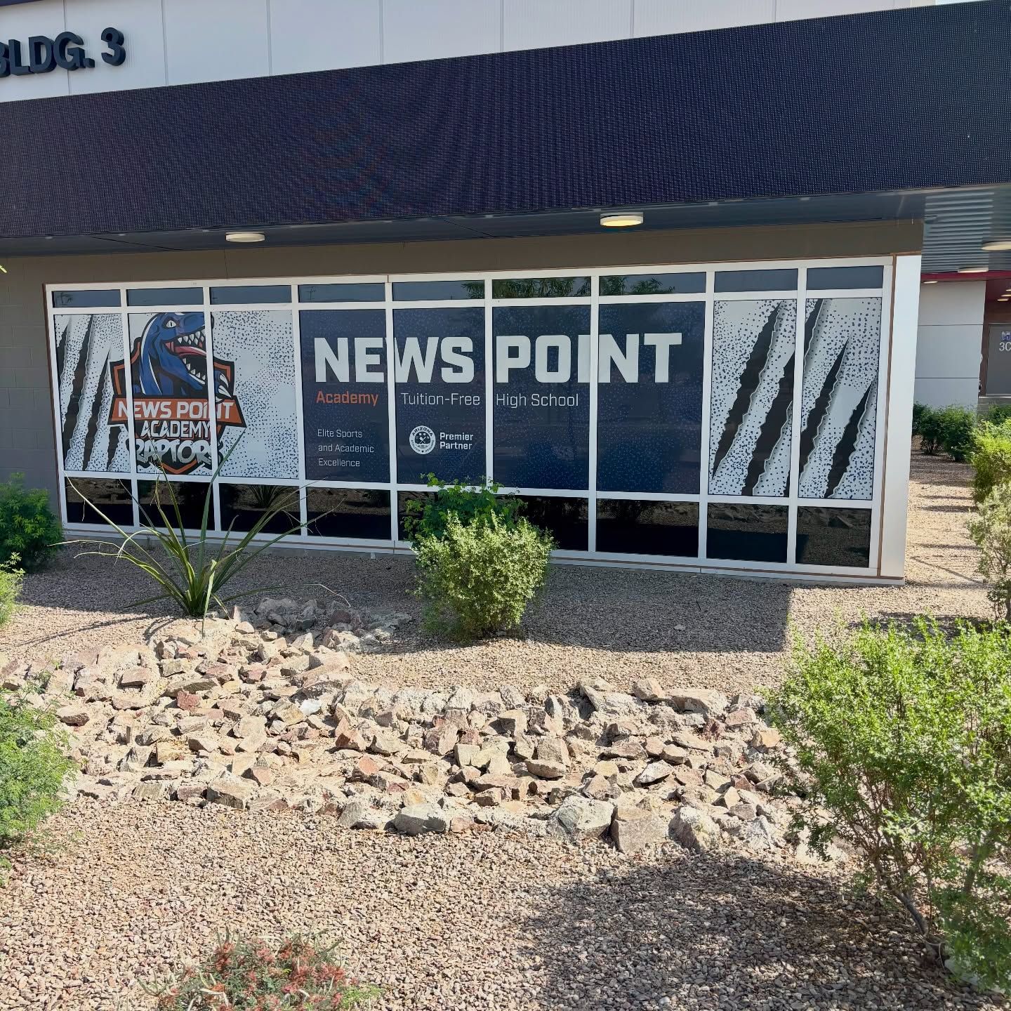 Storefront window with “NEWS POINT” sign and desert landscaping outside