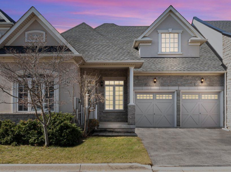 Exterior view of a bungalow townhouse with a driveway, garage, and lawn. Twilight sky.