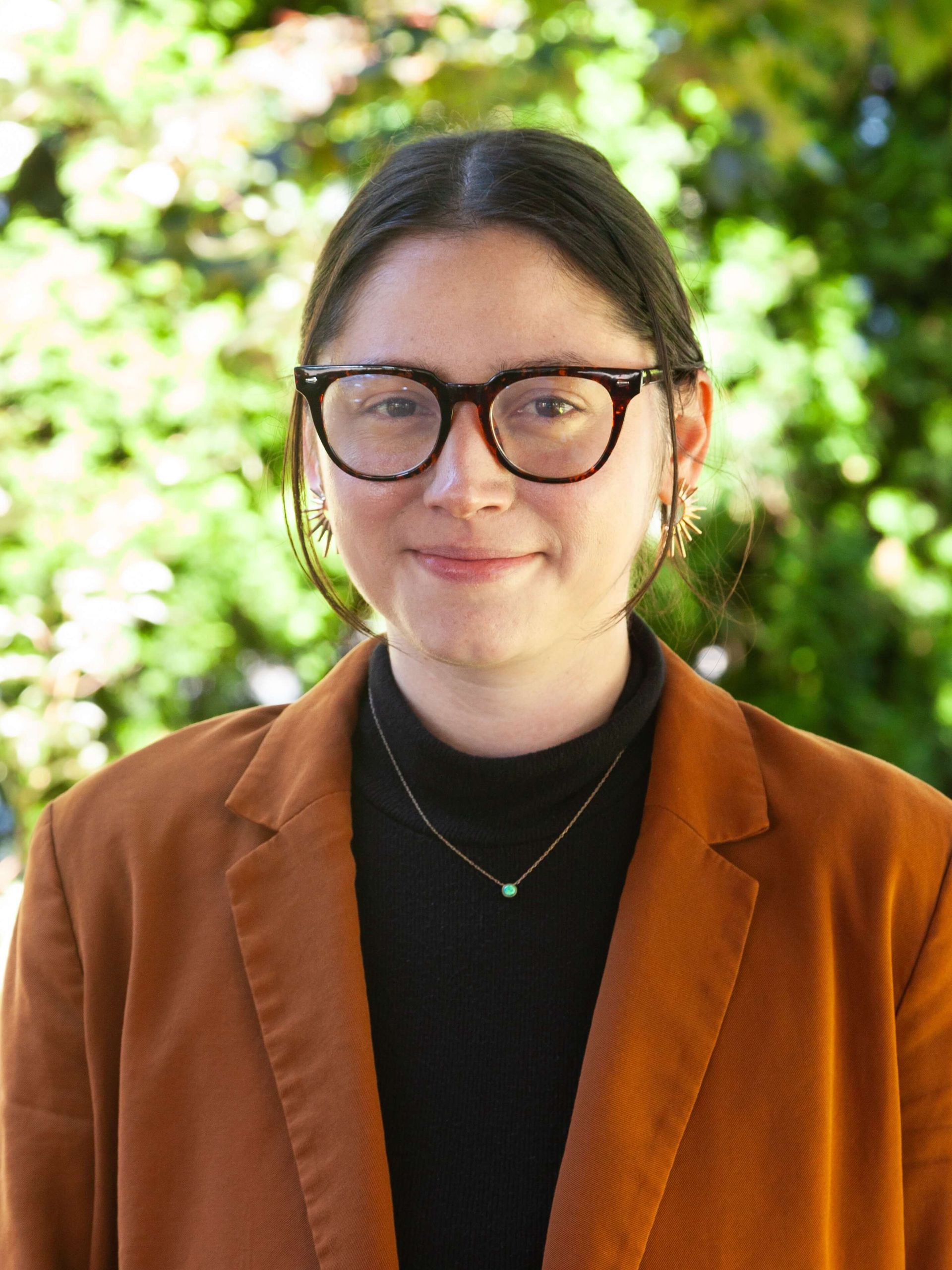Woman wearing glasses and an orange blazer smiling.