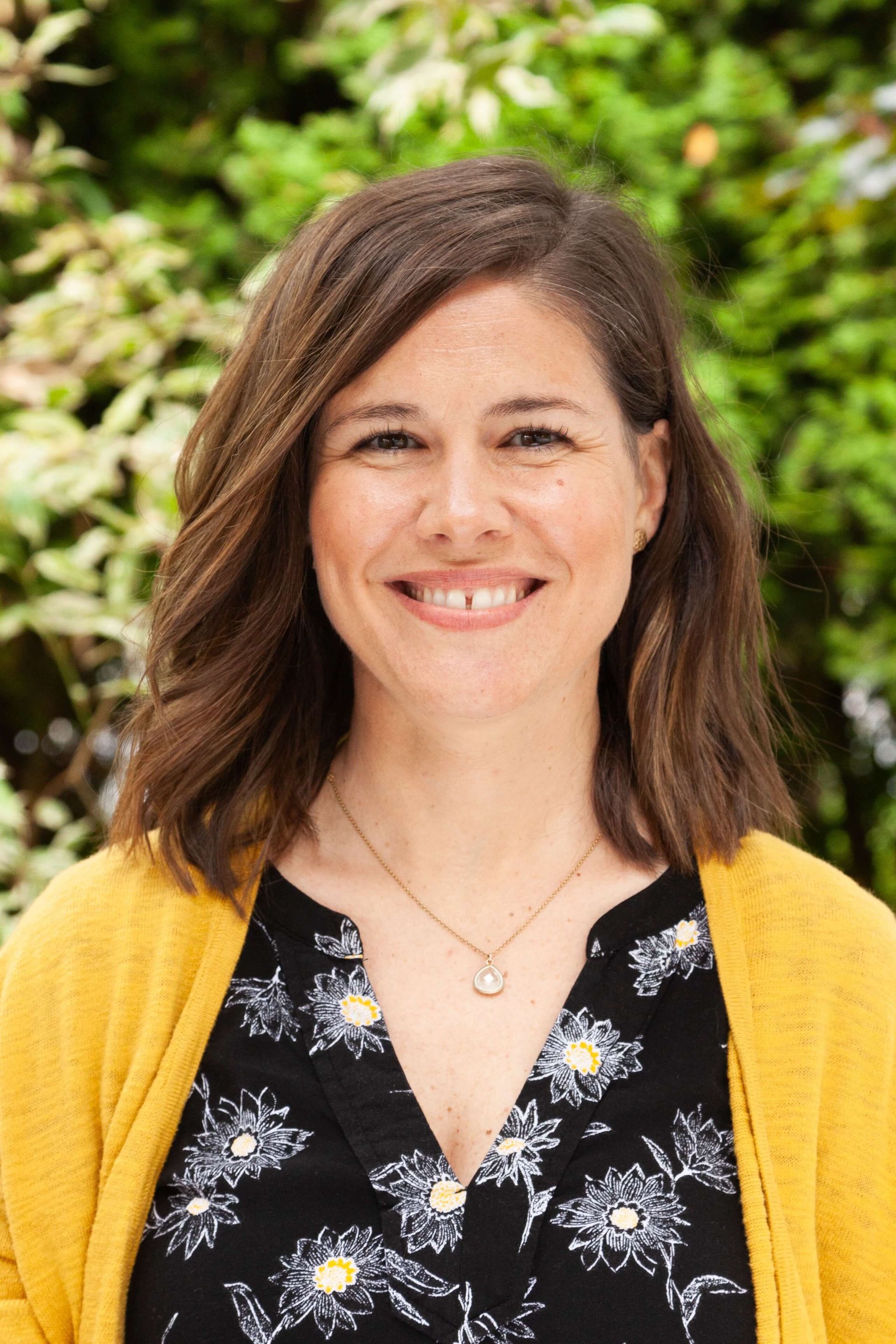 Woman smiling wearing a yellow cardigan. 