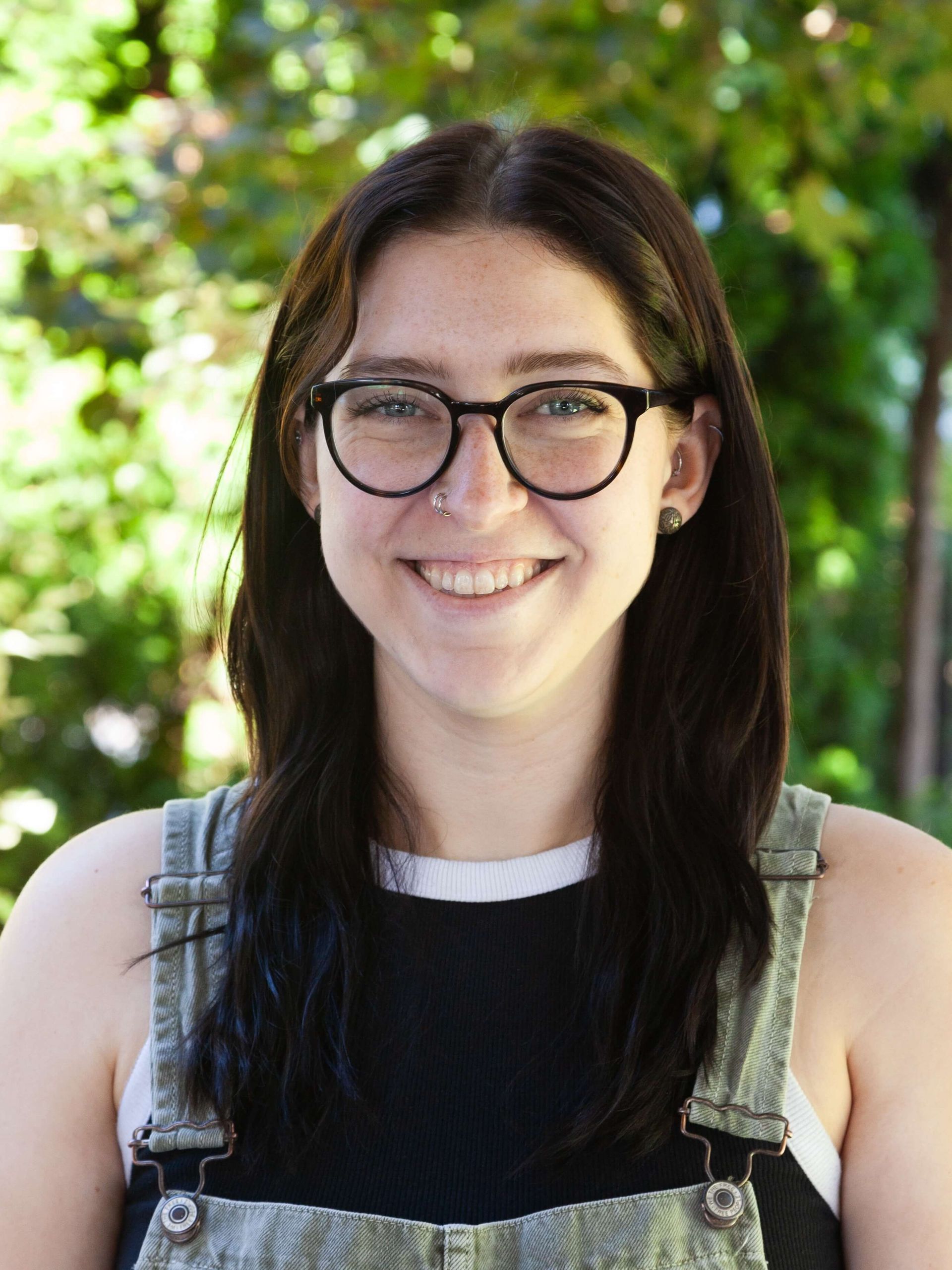 Woman smiling and wearing glasses and overalls. 
