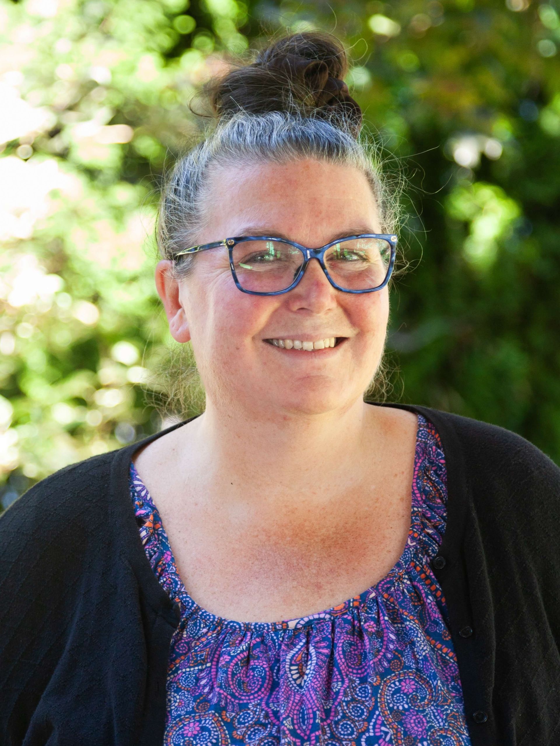 A woman smiling with her hair up and glasses on. 