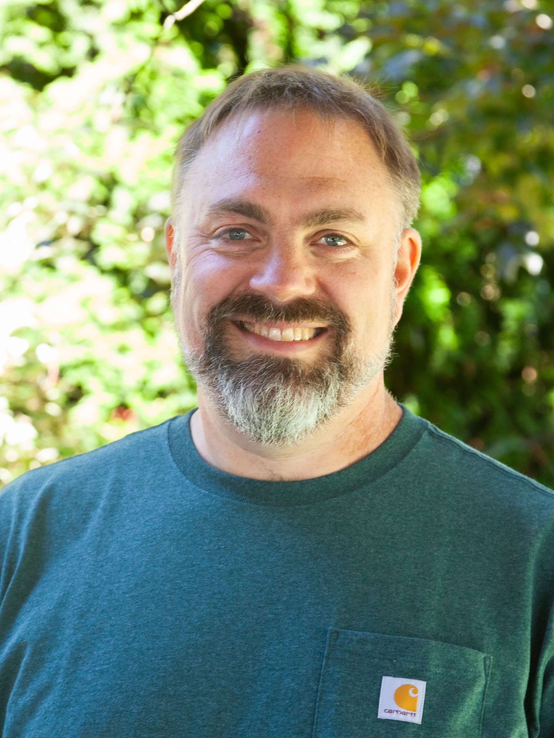 Mane smiling in dark green tee shirt and some facial hair.
