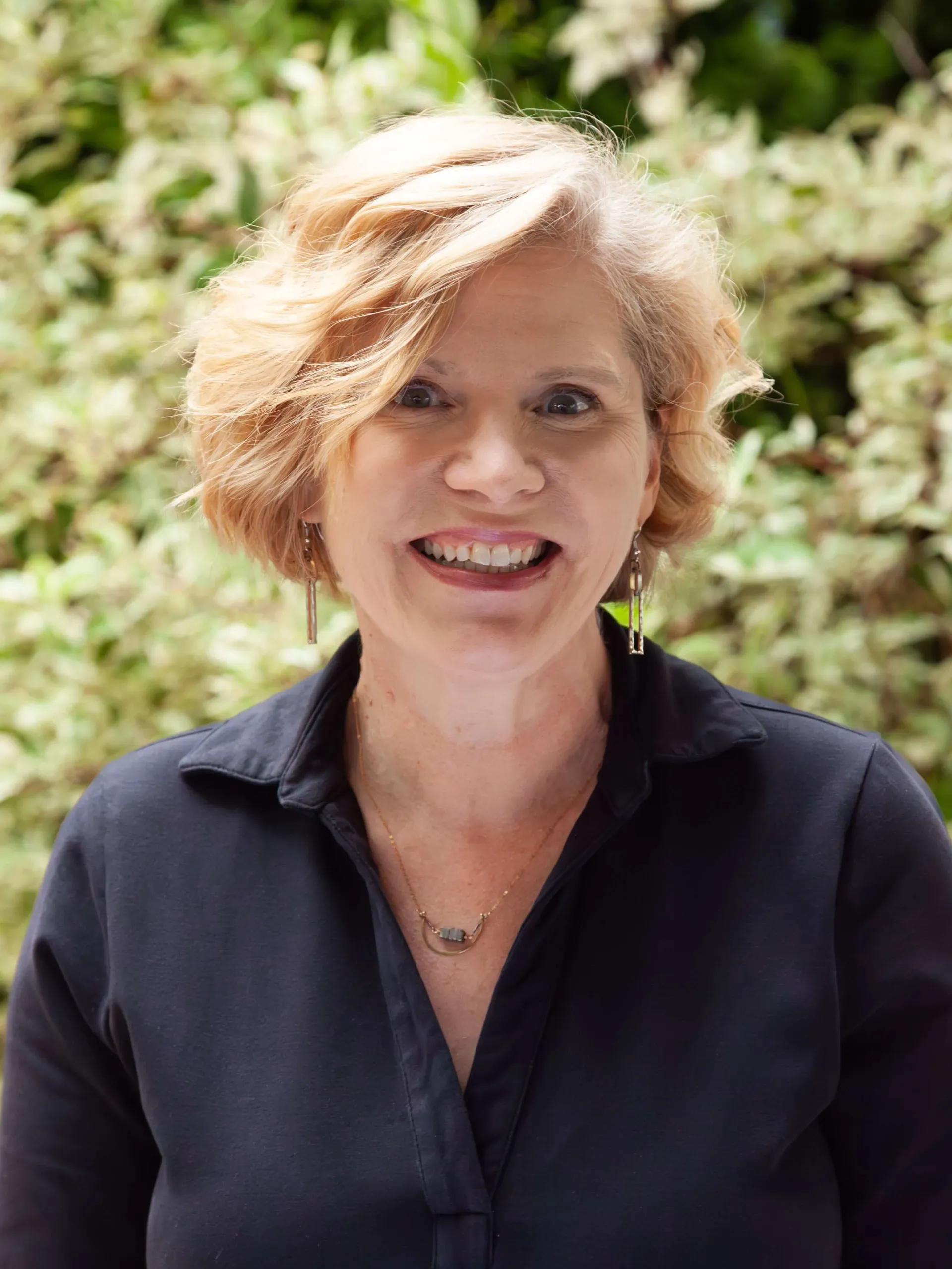A woman wearing glasses and a black shirt is smiling in a black and white photo.