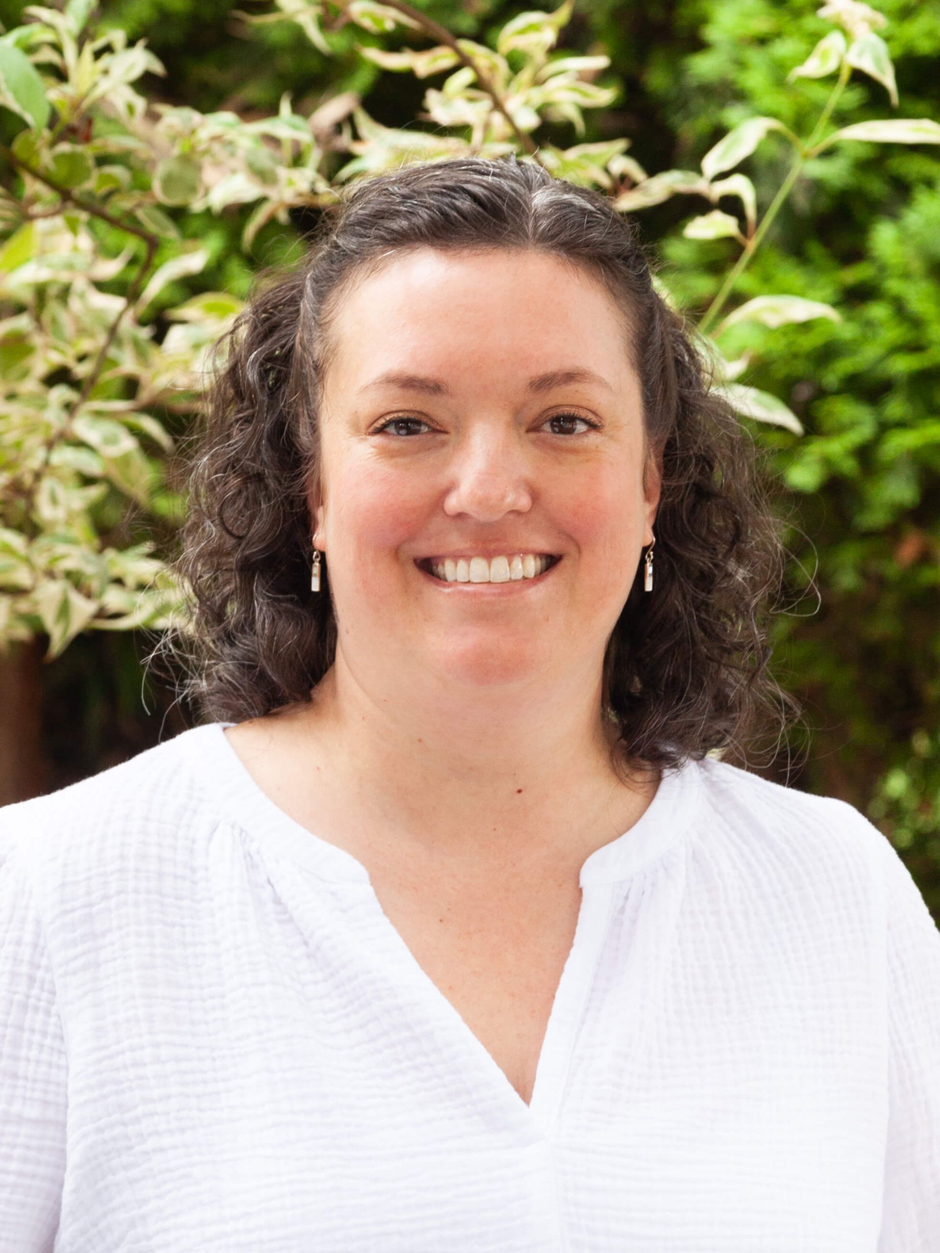 Woman in white blouse and medium length curly brown hair. 