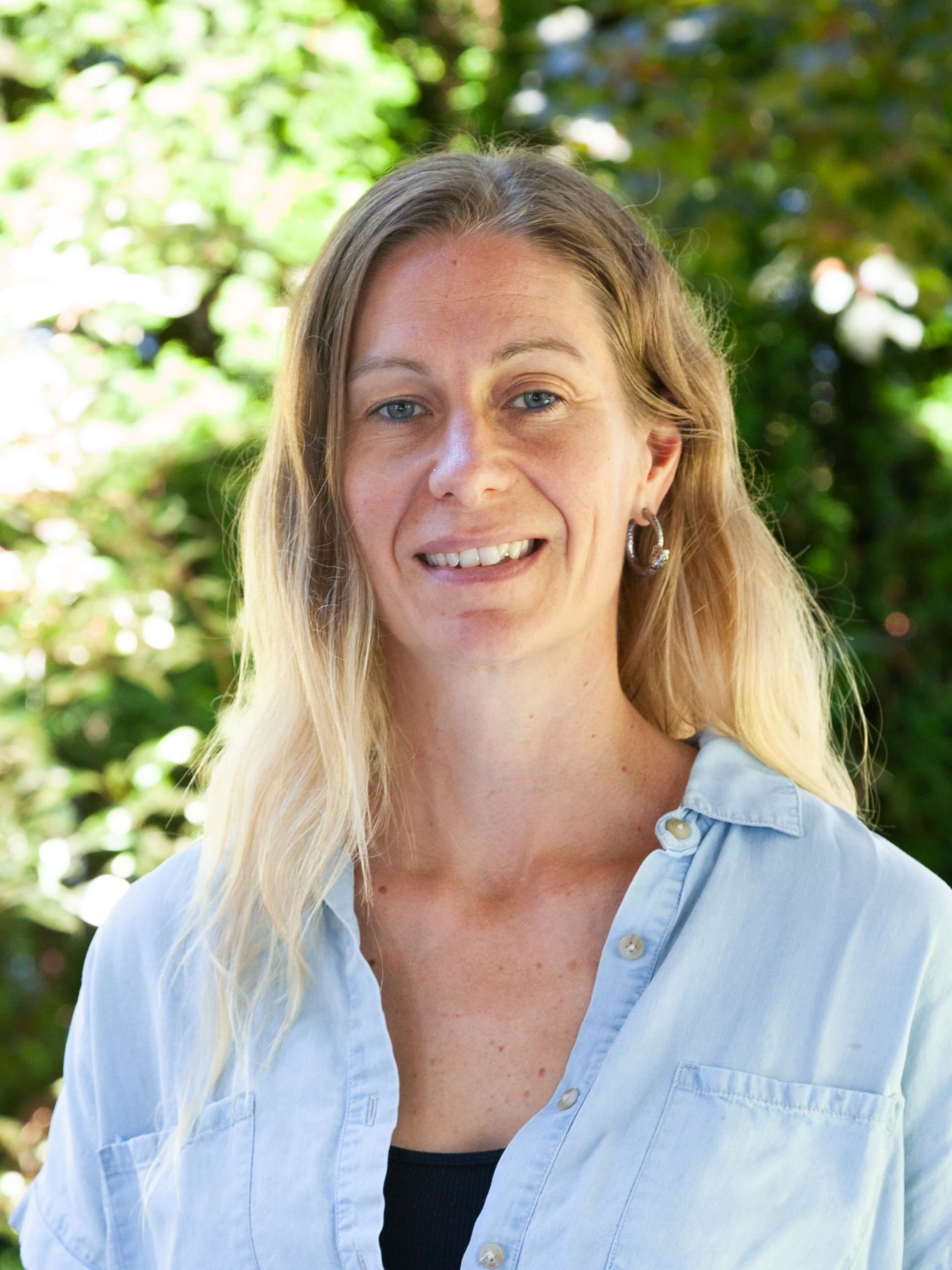 Woman gently smiling with pale blue collared shirt. 
