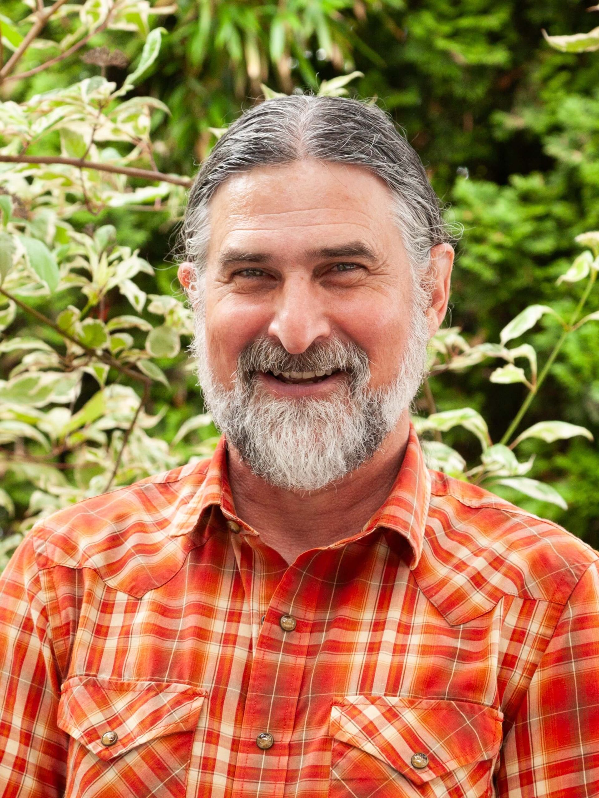 Man smiling in plaid collared shirt and facial hair. 