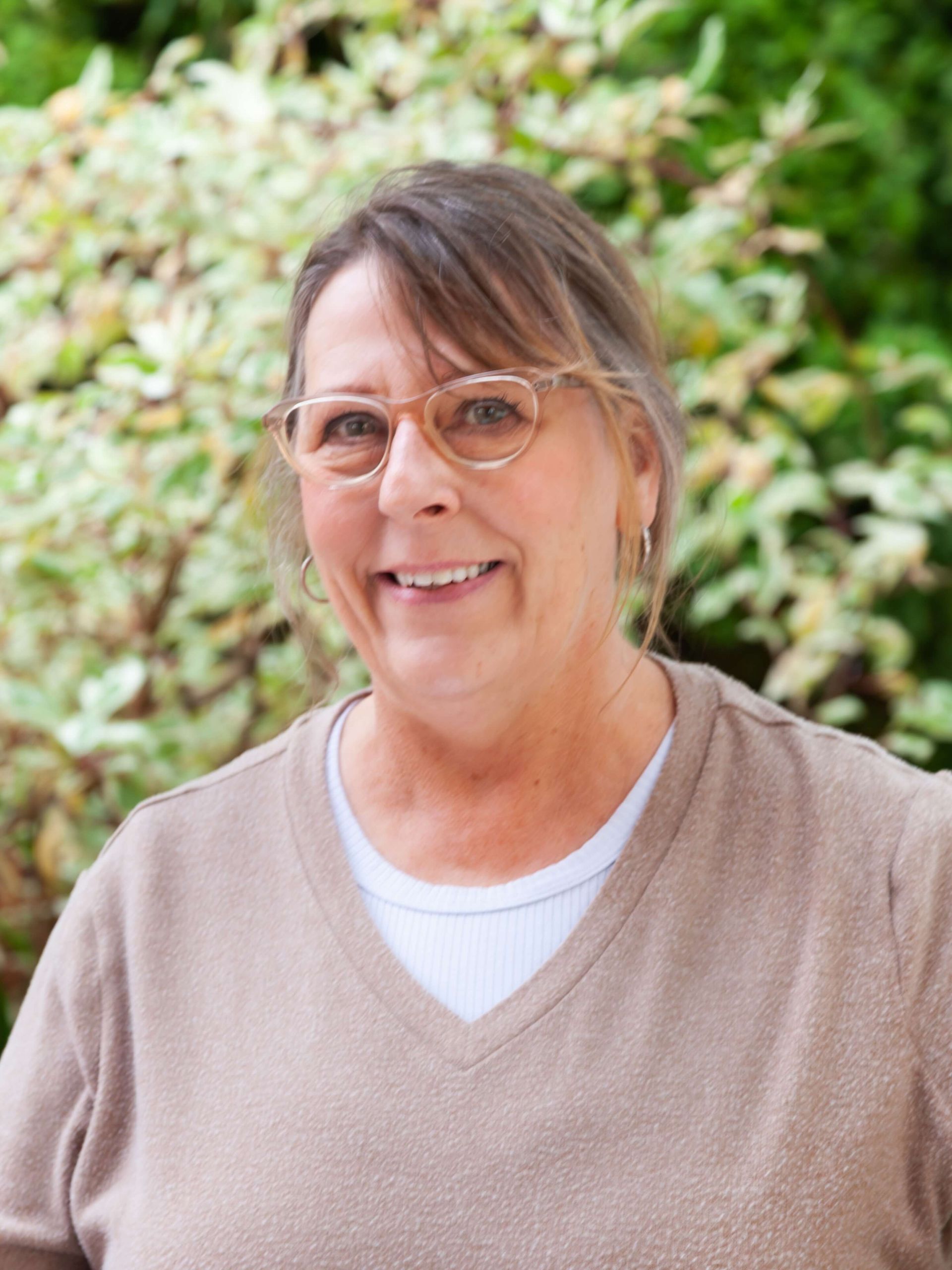 Woman in tan sweater and wearing glasses.