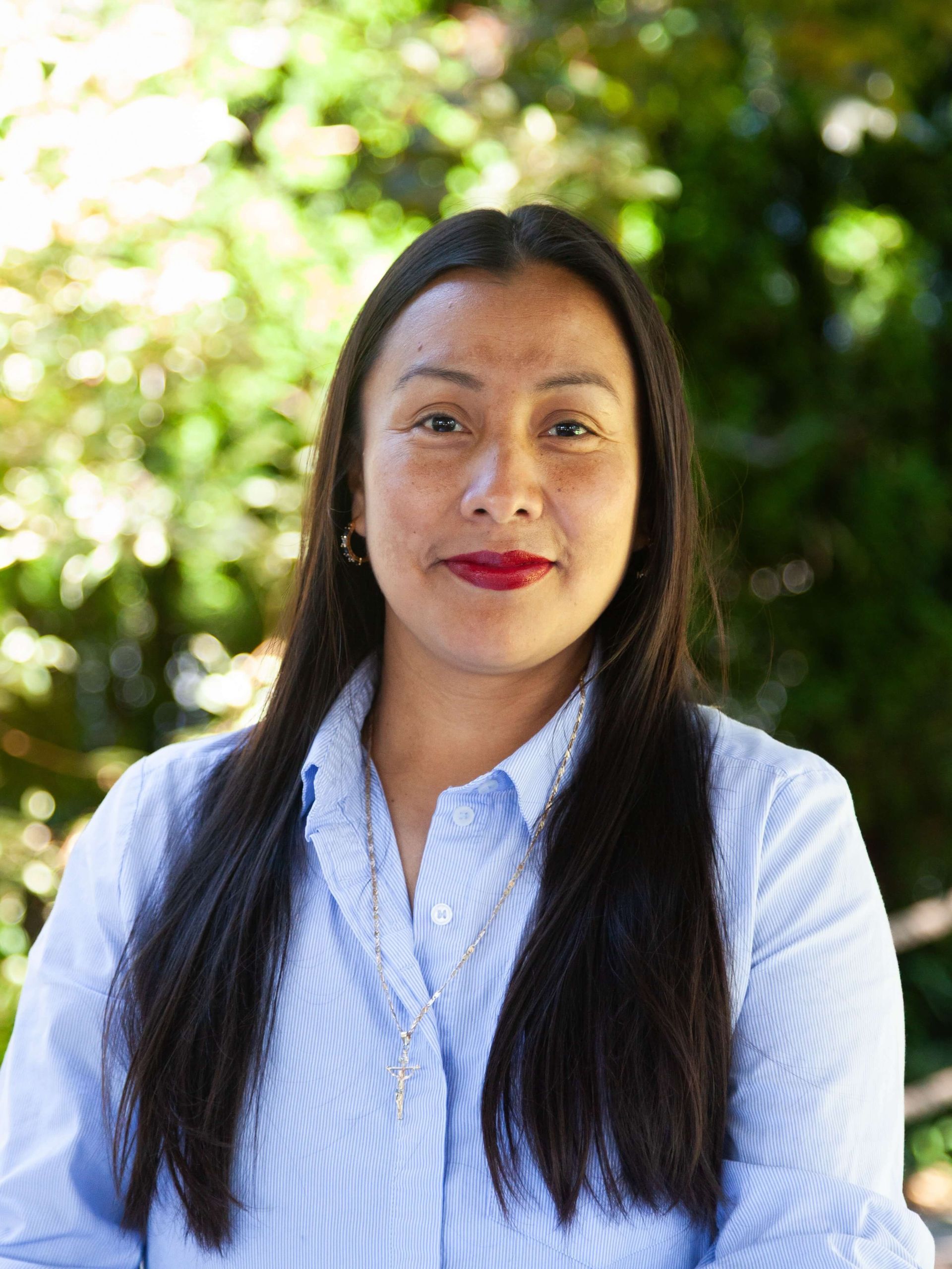 Woman smiling gently with red lipstick and long black hair.