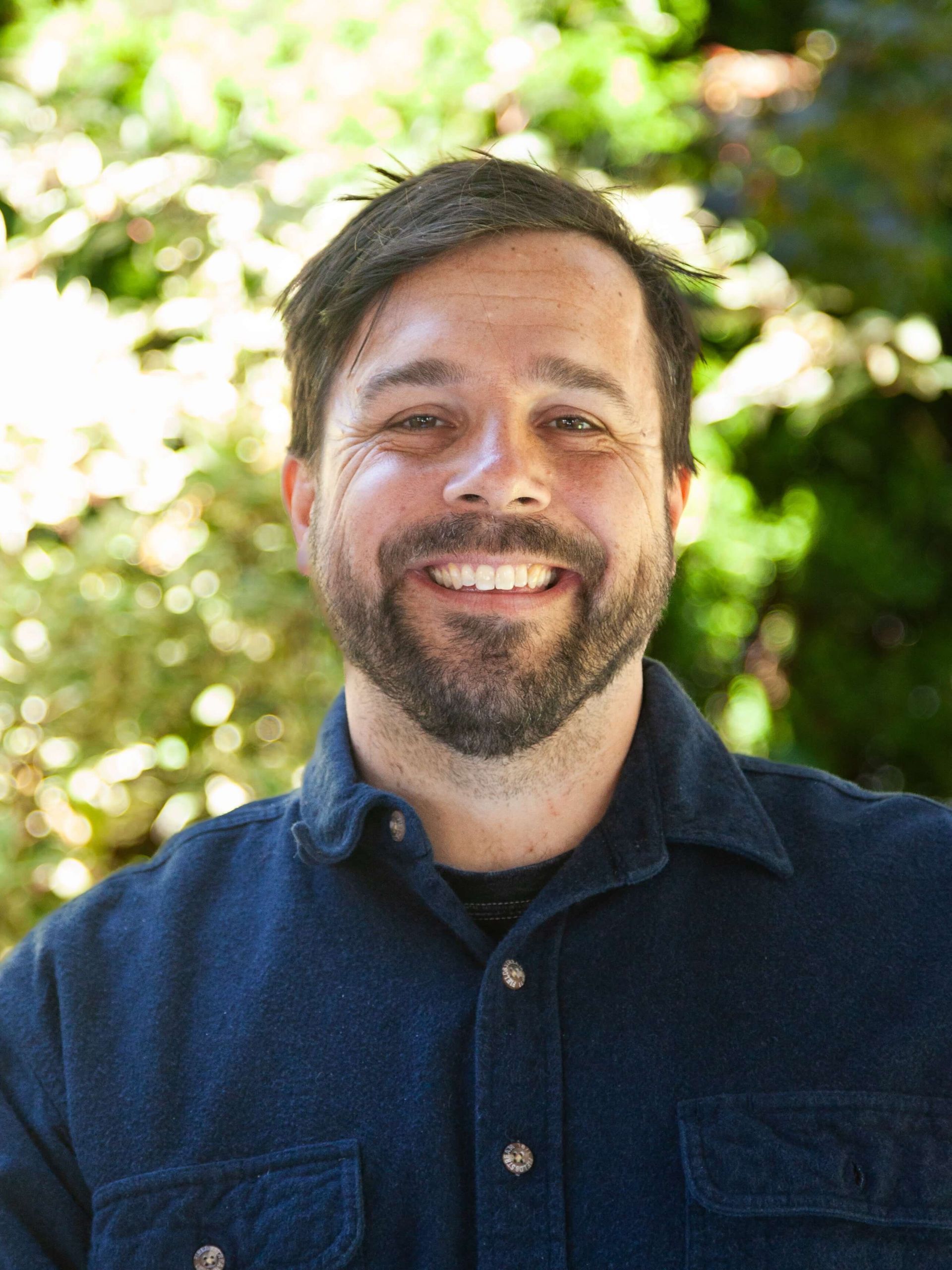 Man smiling in collared shirt and facial hair. 