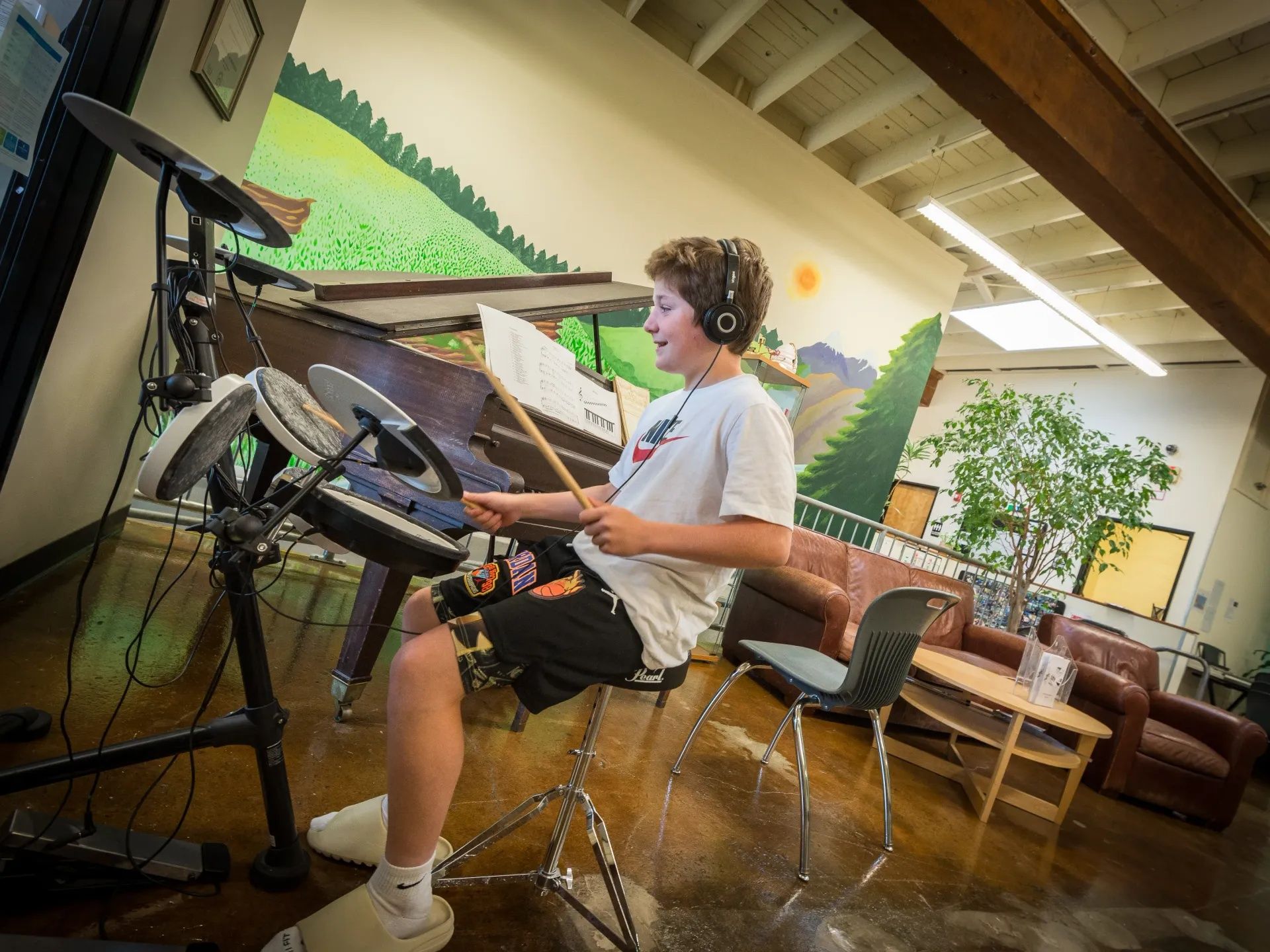 Middle school aged kid, wearing headphones and playing on an electronic drum set.
