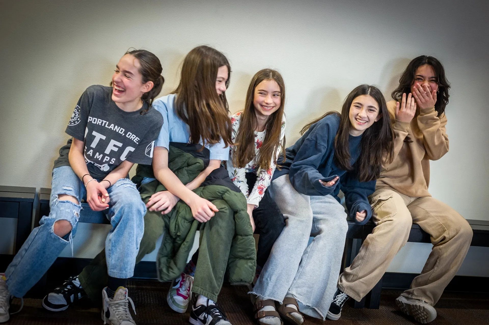 Five upper elementary girls sitting on bench together and laughing.