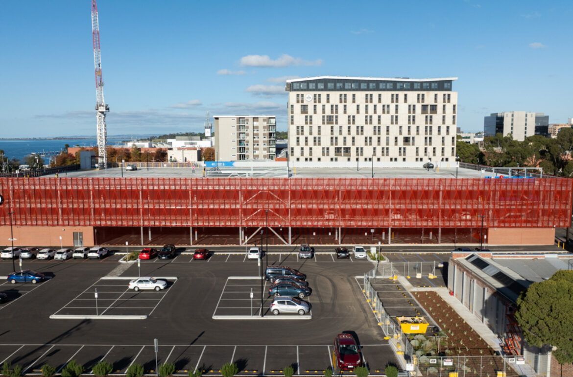 An aerial view on red building of a parking lot in front of a large building.