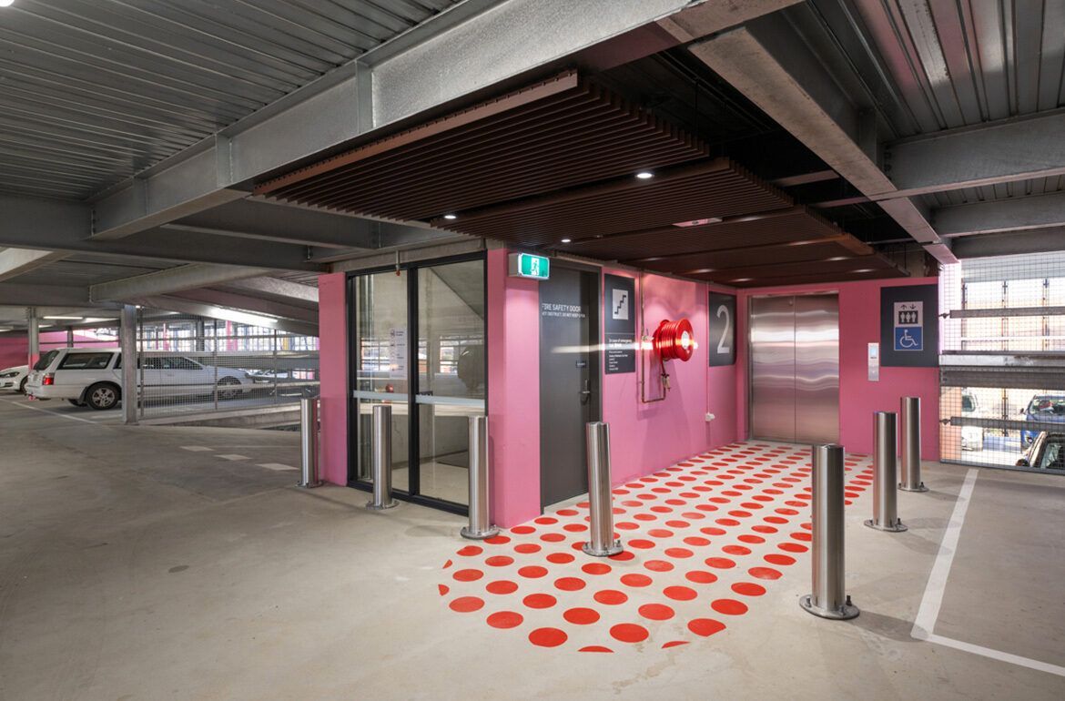 A parking garage with pink walls and red polka dots on the floor.