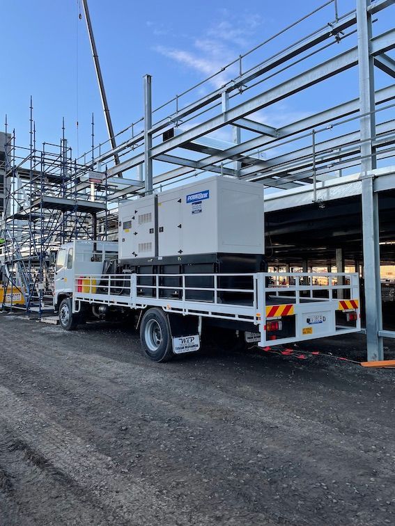A white truck with generator is parked in front of a building under construction.
