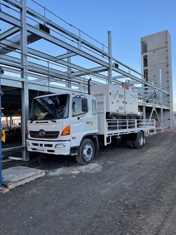 A white truck is parked in front of a building under construction with generator