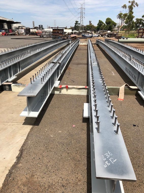 A bunch of steel beams are sitting on the ground with big nails on it