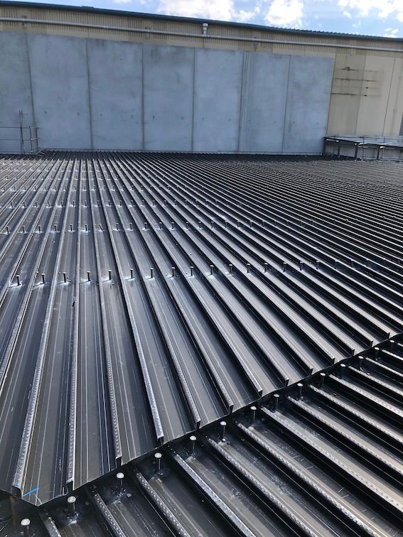 A close up of a black metal roof with a concrete wall in the background.